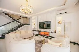 Luxury family lounge at J & M Palms Residence Nairobi with modern curved sofas, fireplace TV wall and glass staircase backdrop.